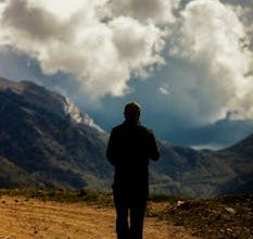 Silhouette of a man hiking on a dirt path with dramatic clouds over Turkish mountains.