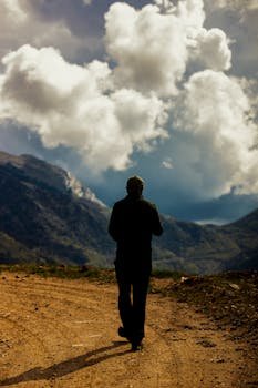 Silhouette of a man hiking on a dirt path with dramatic clouds over Turkish mountains.